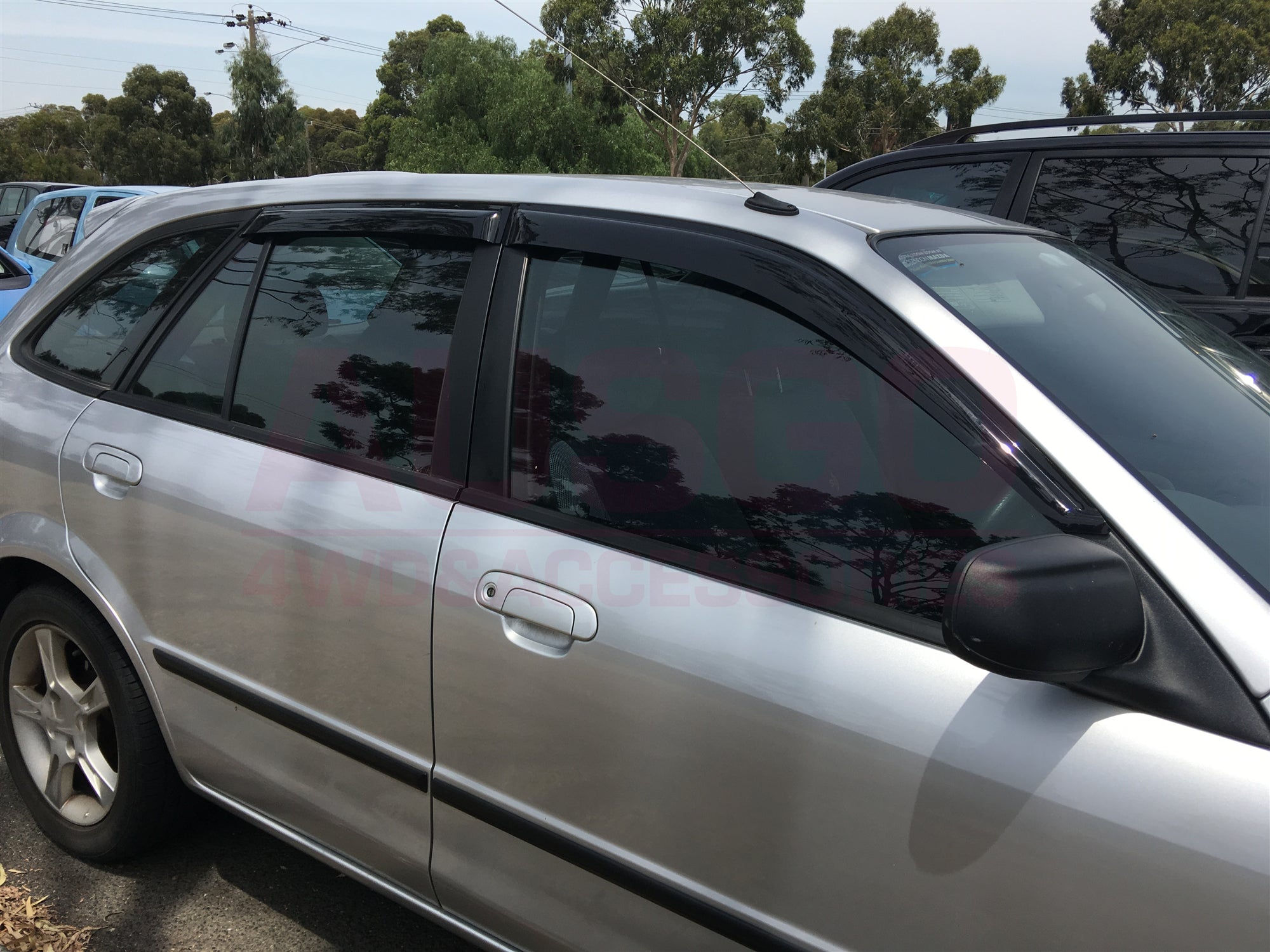 Side view of a grey Ford Laser with black weather shields attached to the windows.