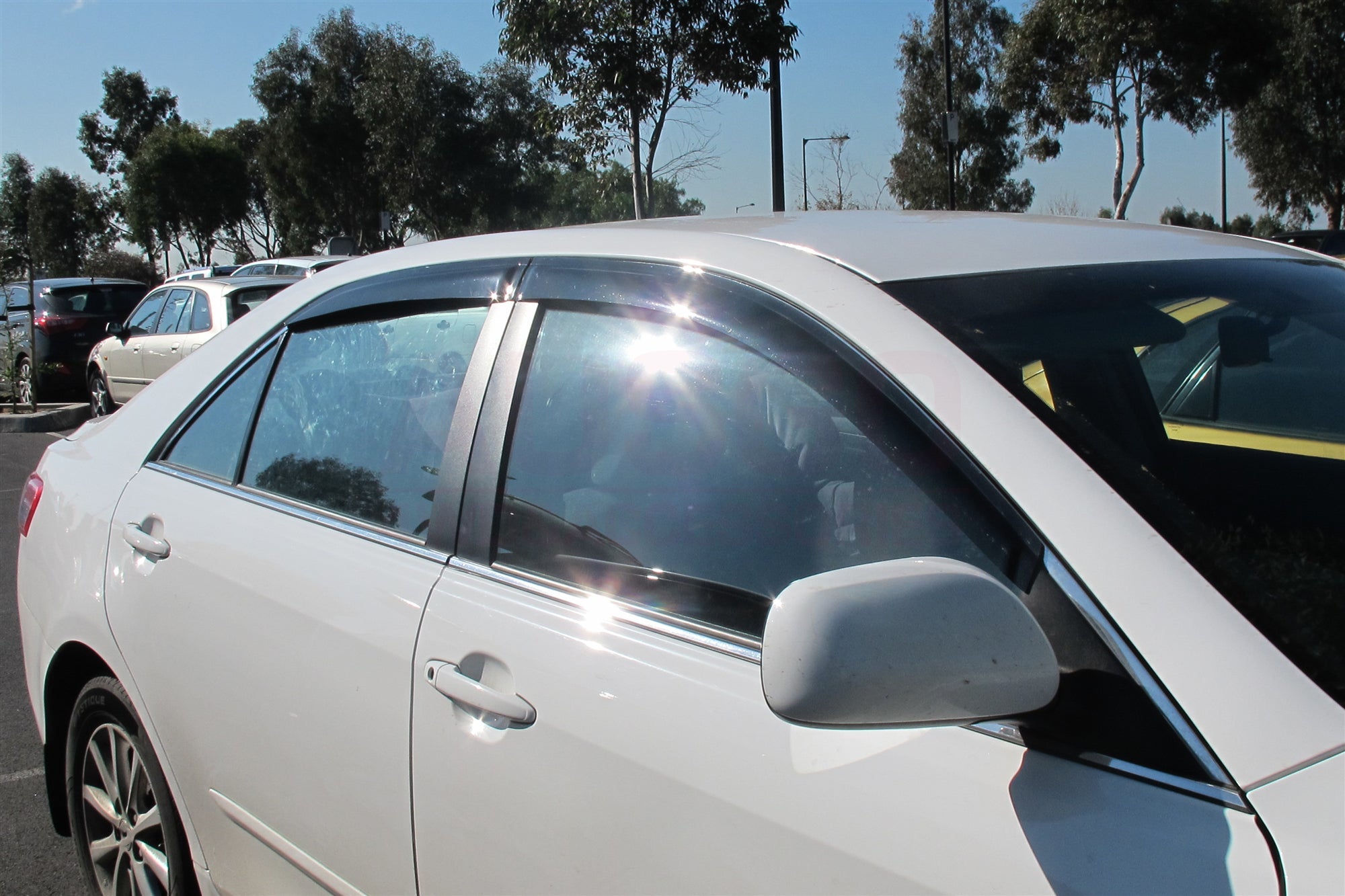 A side view of a white Toyota Camry parked in an outdoor carpark on a sunny day.