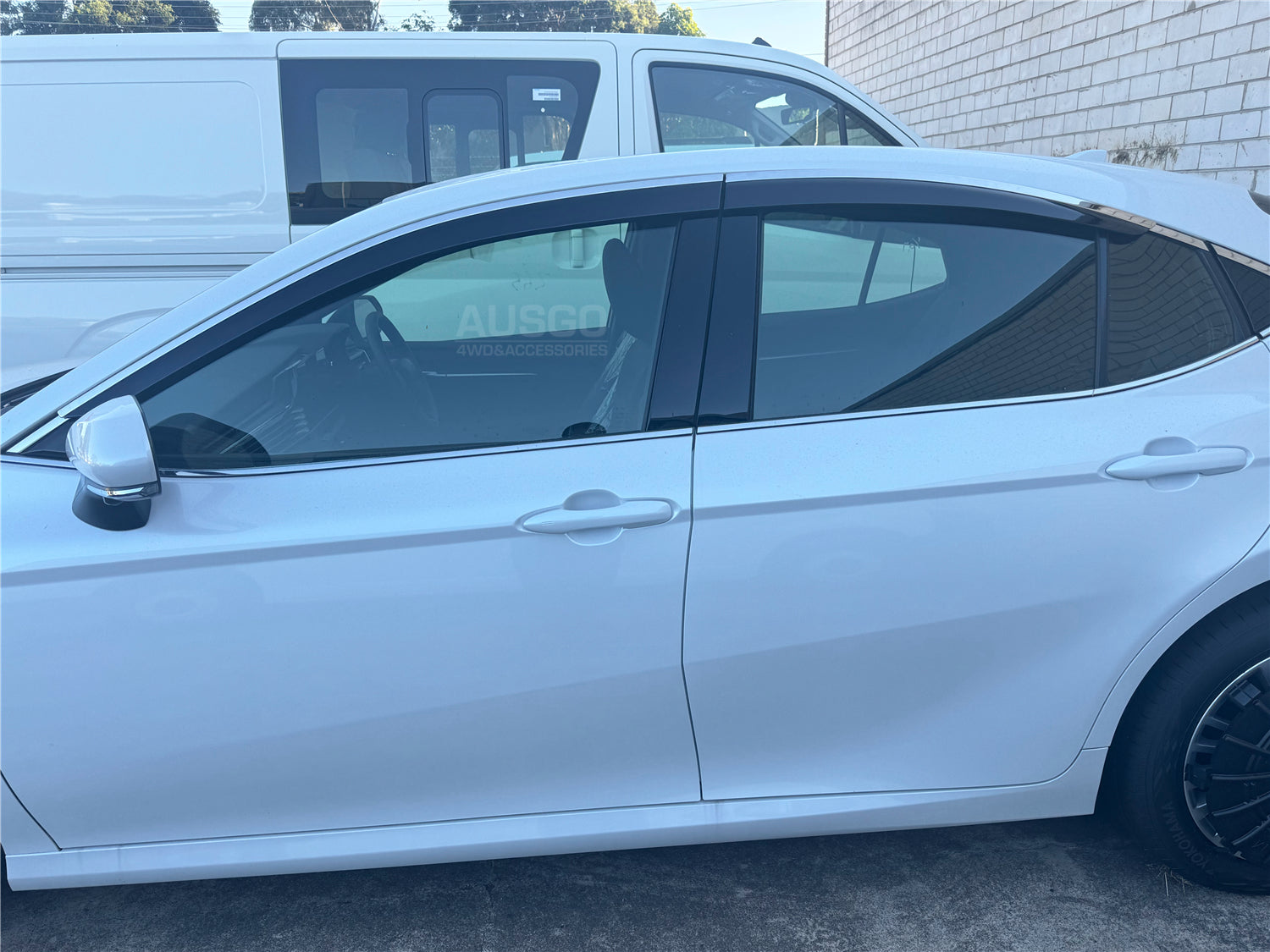 Side view of a Toyota Camry parked in an outdoor car park next to a van.