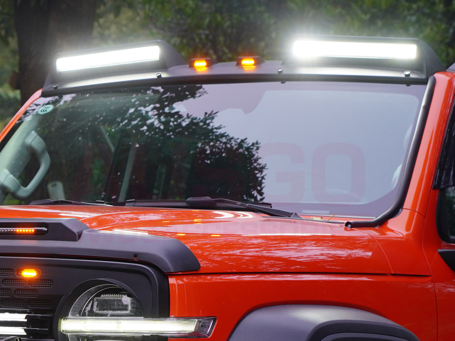 Front view of an orange 4x4 with Ausgo roof searchlights, illuminating the windshield area for off-road visibility