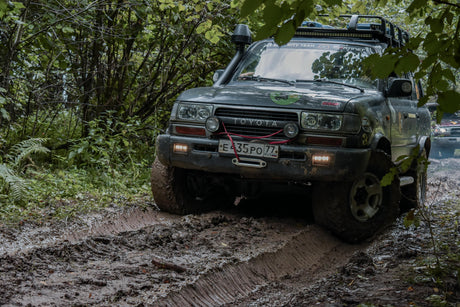 Toyota Land Cruiser navigating a muddy forest trail, equipped with off-road accessories for rugged 4WD adventure