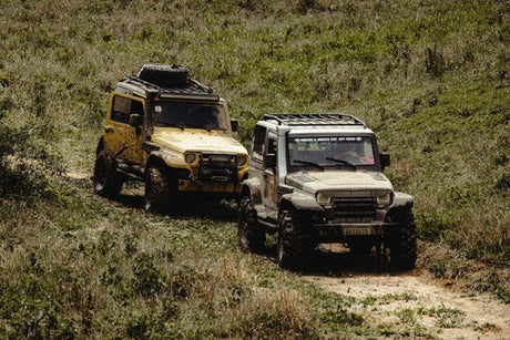 Two off-road vehicles covered in mud driving through grassy terrain, showcasing an adventurous off-road journey.