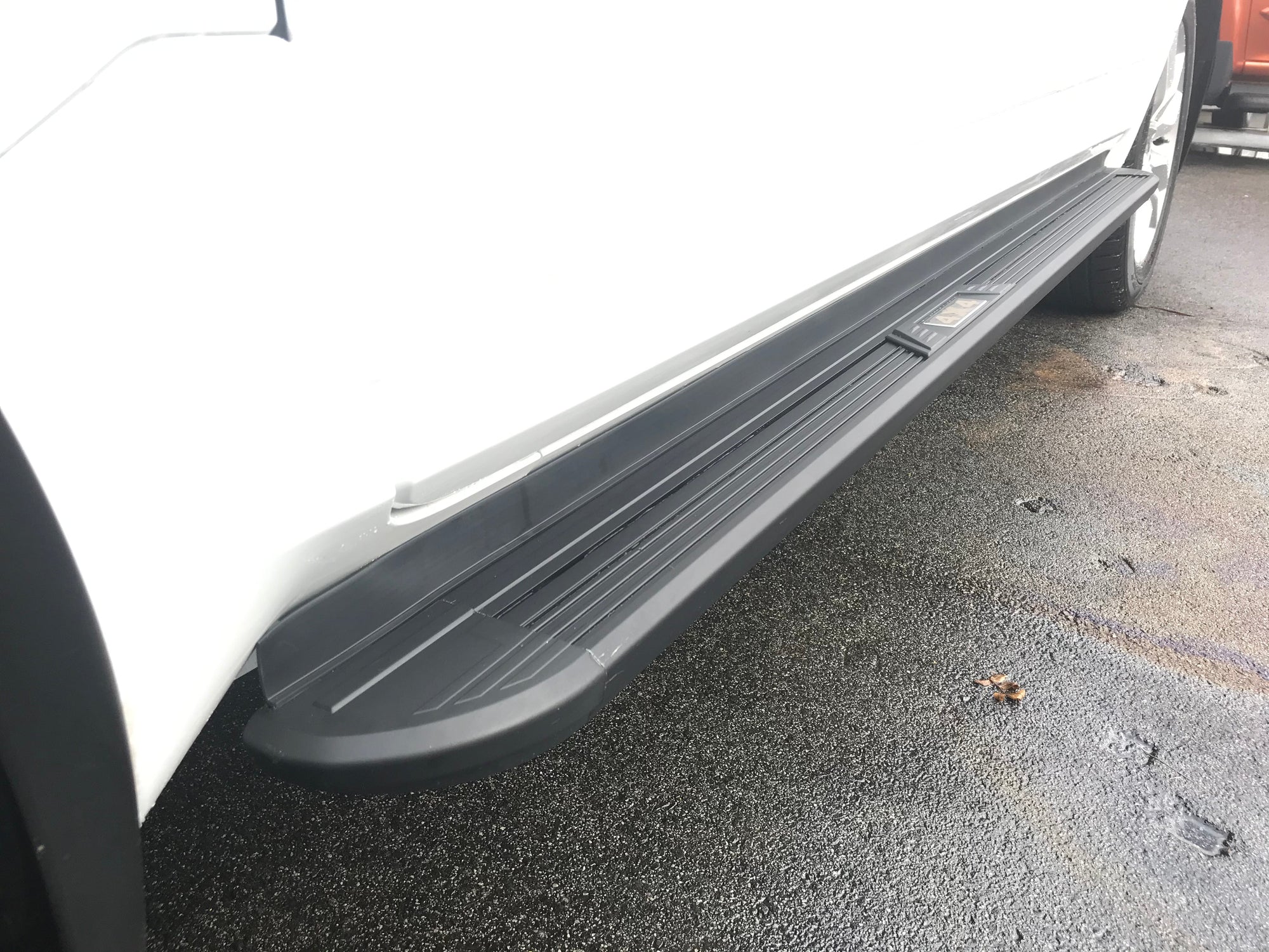 Zoomed in photo of black side steps on a white car. 